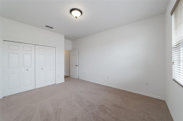 unfurnished bedroom with multiple windows, light carpet, and a closet