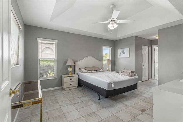 bedroom featuring light tile patterned flooring, multiple windows, ceiling fan, and a tray ceiling