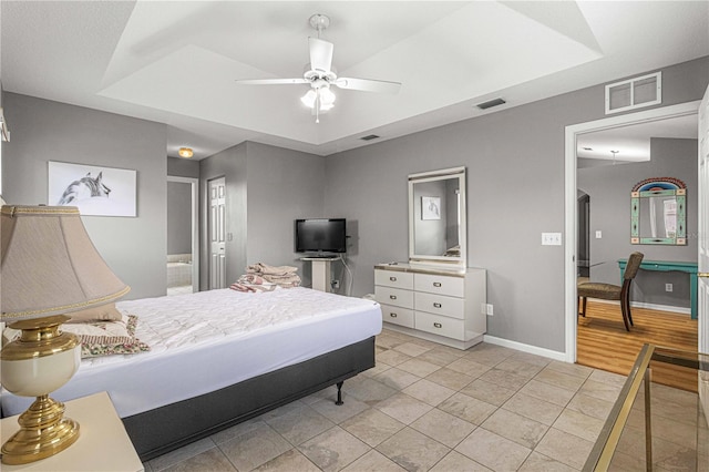 bedroom with light hardwood / wood-style floors, ceiling fan, and a raised ceiling