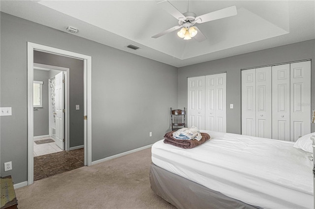 tiled bedroom featuring two closets, ceiling fan, and a raised ceiling