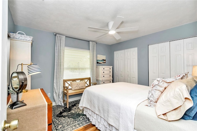 bedroom featuring ceiling fan, two closets, a textured ceiling, and hardwood / wood-style flooring