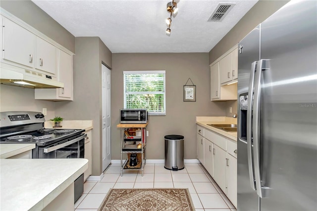 kitchen with sink, light tile patterned flooring, stainless steel appliances, a textured ceiling, and white cabinets