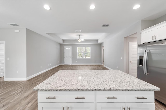 kitchen featuring light stone counters, ceiling fan, stainless steel fridge, and white cabinets