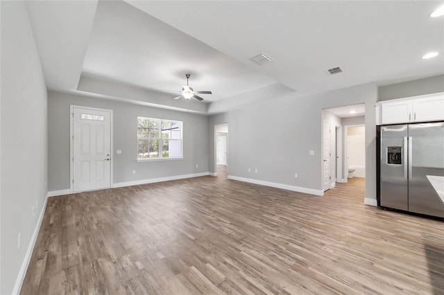 unfurnished living room with a tray ceiling, ceiling fan, and light hardwood / wood-style floors