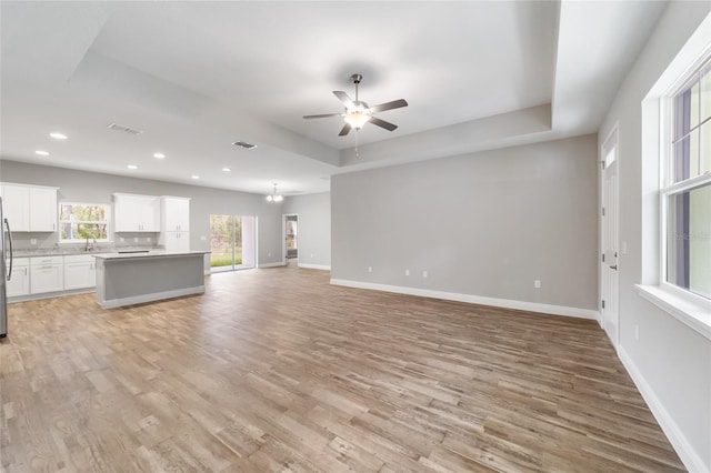 unfurnished living room with a tray ceiling, light hardwood / wood-style floors, and ceiling fan