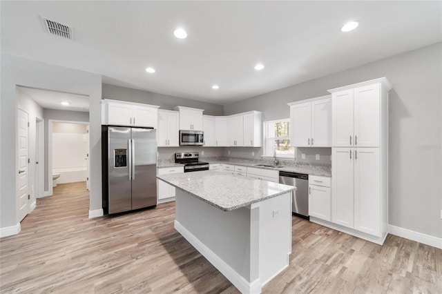 kitchen with sink, stainless steel appliances, a center island, light stone countertops, and white cabinets