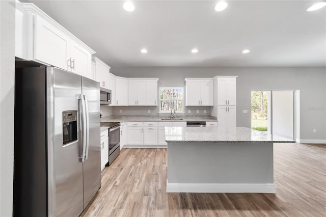 kitchen with white cabinetry, stainless steel appliances, a center island, light stone counters, and light wood-type flooring