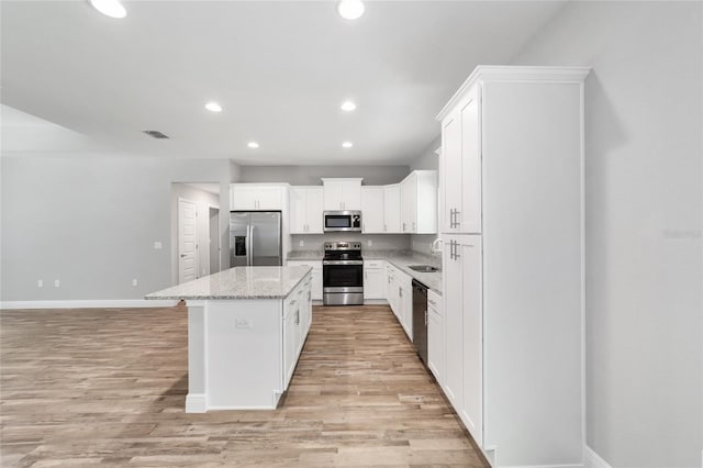 kitchen featuring a kitchen island, white cabinets, stainless steel appliances, light stone countertops, and light wood-type flooring