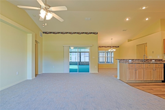 unfurnished living room with ceiling fan with notable chandelier, light colored carpet, vaulted ceiling, and sink