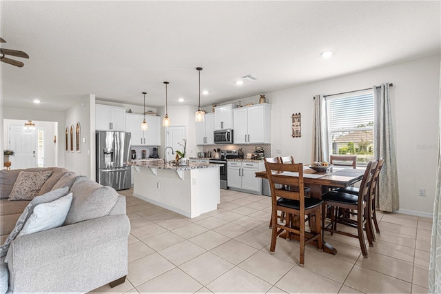 interior space with decorative light fixtures, an island with sink, white cabinets, and appliances with stainless steel finishes