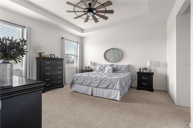 bedroom with a tray ceiling, light colored carpet, and ceiling fan