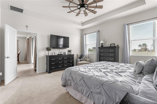 carpeted bedroom with a raised ceiling and ceiling fan