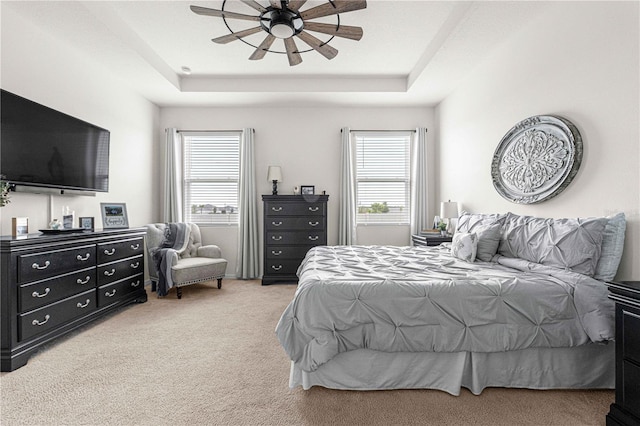 carpeted bedroom featuring ceiling fan, a tray ceiling, and multiple windows