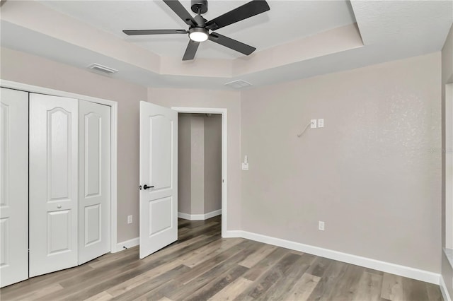 unfurnished bedroom with a raised ceiling, ceiling fan, a closet, and hardwood / wood-style floors