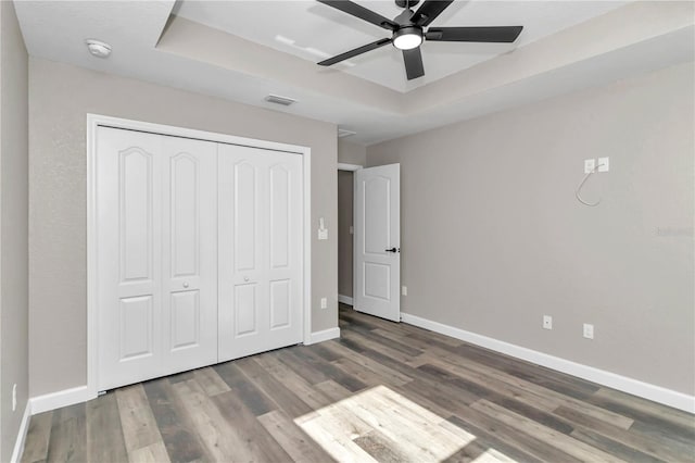 unfurnished bedroom with a raised ceiling, ceiling fan, a closet, and wood-type flooring