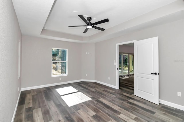 unfurnished room featuring a tray ceiling, ceiling fan, and dark wood-type flooring