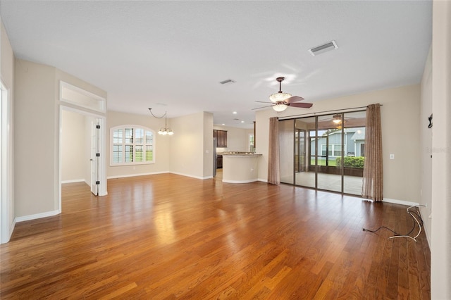 unfurnished living room featuring ceiling fan with notable chandelier and wood-type flooring