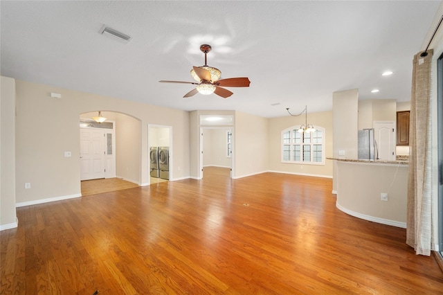 unfurnished living room with ceiling fan with notable chandelier, light hardwood / wood-style floors, and washer and dryer