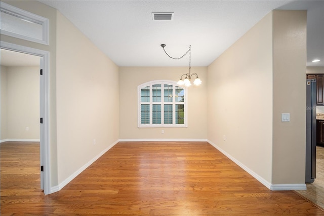 spare room featuring light wood-type flooring and an inviting chandelier