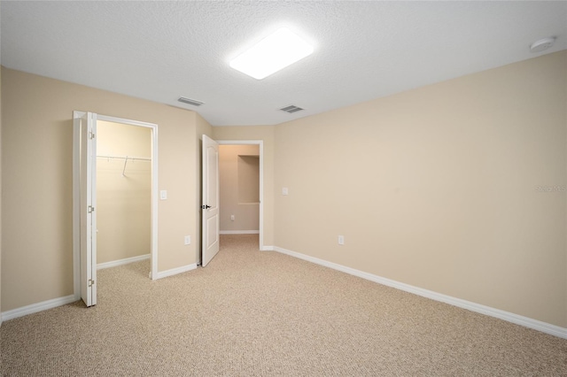 unfurnished bedroom with a textured ceiling, light colored carpet, a closet, and a walk in closet