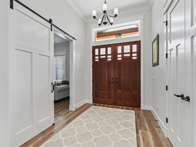 entryway with an inviting chandelier, crown molding, wood-type flooring, and a barn door