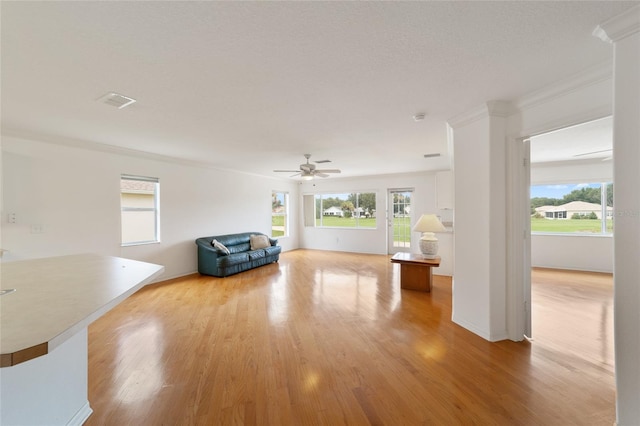 unfurnished living room with a wealth of natural light, ornamental molding, ceiling fan, and light wood-type flooring