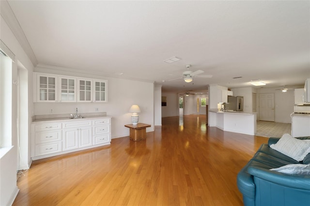 unfurnished living room featuring wet bar, ornamental molding, light hardwood / wood-style floors, and ceiling fan