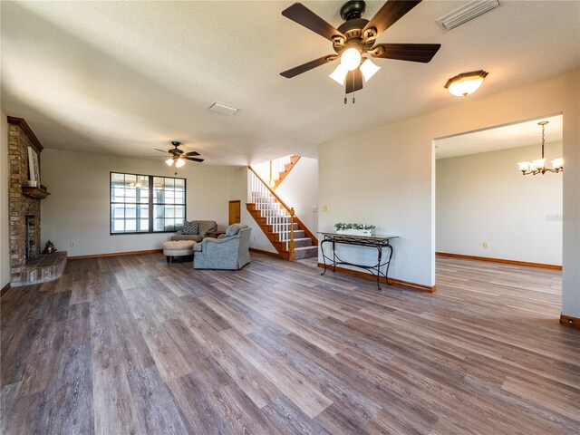 unfurnished room featuring a fireplace, ceiling fan with notable chandelier, a textured ceiling, and hardwood / wood-style flooring