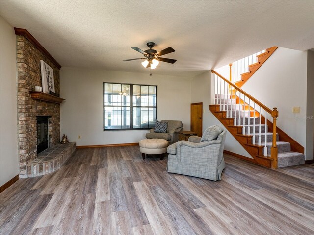 living room with hardwood / wood-style flooring, a textured ceiling, a brick fireplace, brick wall, and ceiling fan