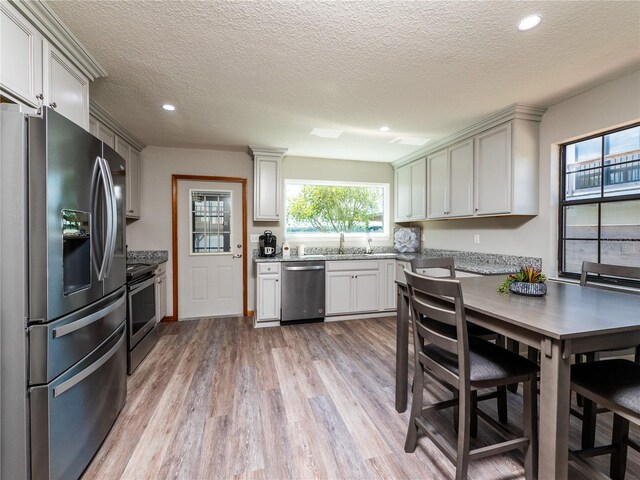 kitchen with appliances with stainless steel finishes, light hardwood / wood-style flooring, white cabinetry, and light stone countertops