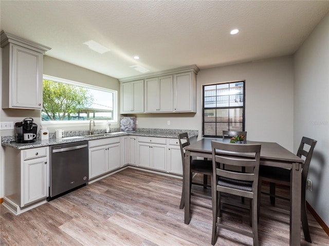 kitchen featuring light hardwood / wood-style flooring, white cabinets, sink, stainless steel dishwasher, and light stone countertops