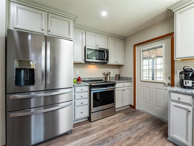 kitchen featuring appliances with stainless steel finishes, white cabinets, light wood-type flooring, light stone countertops, and a textured ceiling