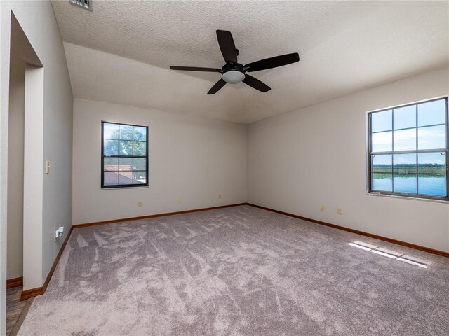 empty room with a water view, a textured ceiling, ceiling fan, and light colored carpet