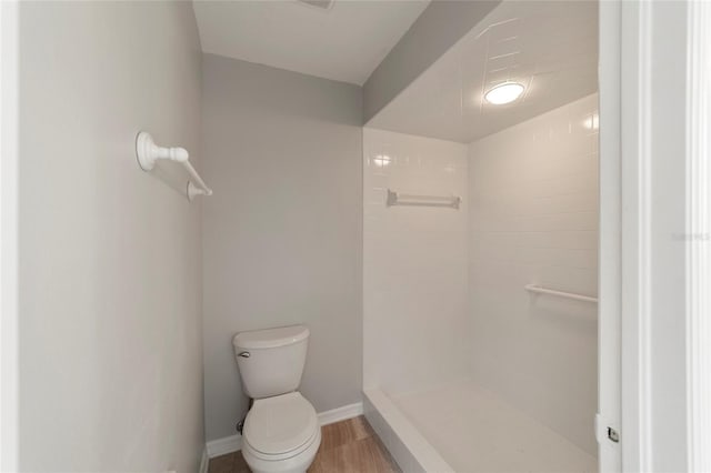 bathroom with hardwood / wood-style flooring, a tile shower, and toilet