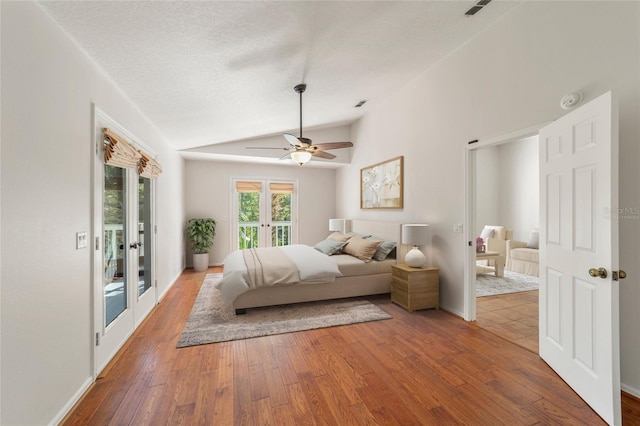 bedroom featuring french doors, vaulted ceiling, a textured ceiling, access to exterior, and hardwood / wood-style floors