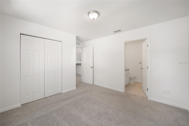 unfurnished bedroom with a closet, light carpet, and ensuite bathroom