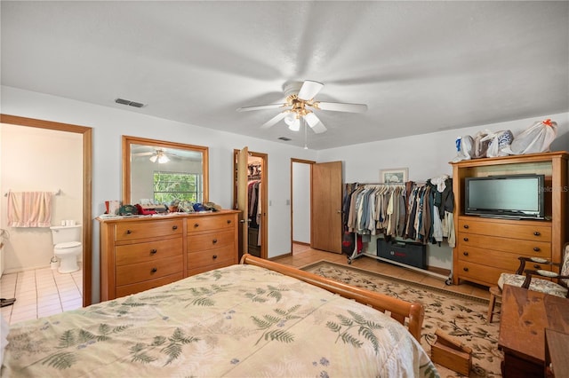 tiled bedroom with ensuite bath, a walk in closet, ceiling fan, and a closet