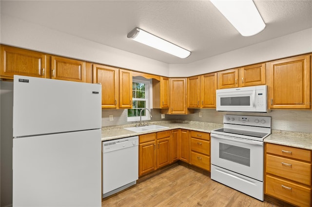 kitchen with sink, light stone countertops, light wood-type flooring, and white appliances