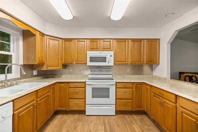 kitchen with sink, light wood-type flooring, light stone counters, and white appliances