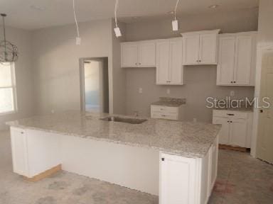 kitchen with white cabinetry, hanging light fixtures, an island with sink, and light stone countertops