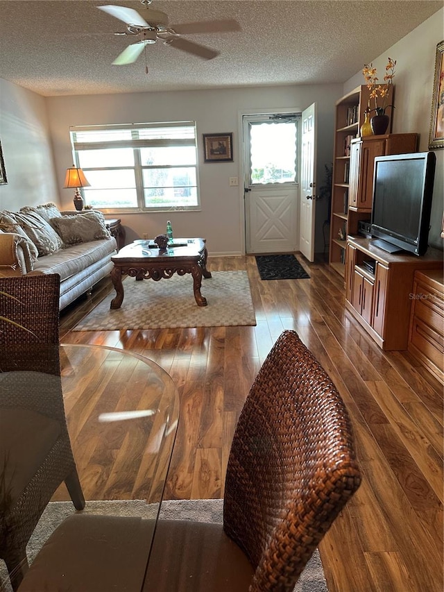 living room with dark wood-type flooring, a textured ceiling, and ceiling fan