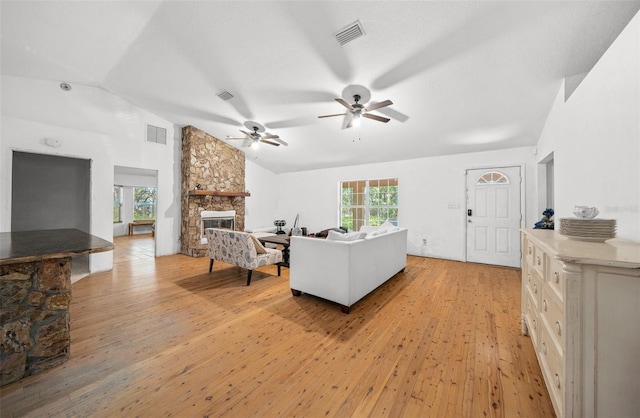 living room with light hardwood / wood-style floors, a wealth of natural light, a stone fireplace, and ceiling fan