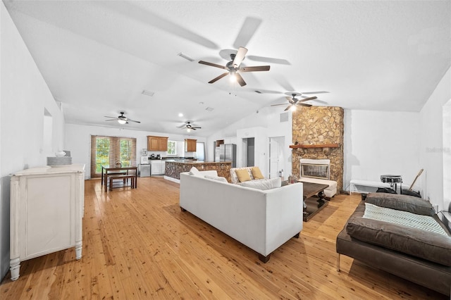 living room featuring a fireplace, vaulted ceiling, light hardwood / wood-style flooring, and ceiling fan