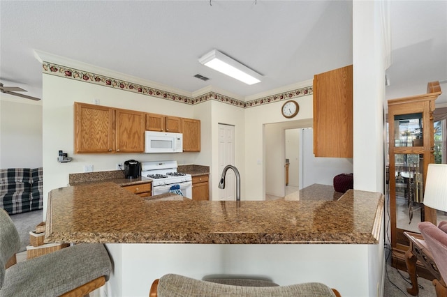 kitchen with white appliances, sink, kitchen peninsula, ceiling fan, and a breakfast bar