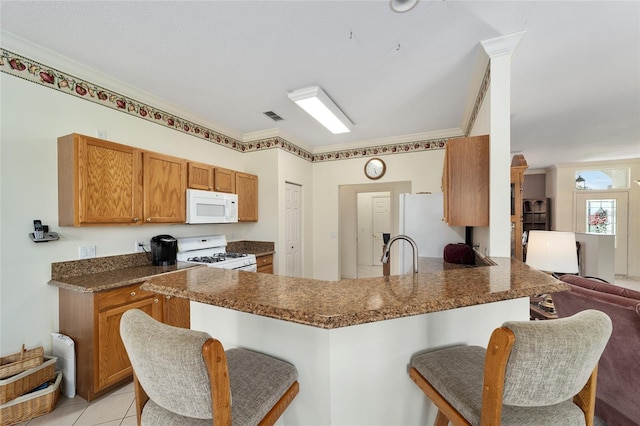 kitchen with light tile patterned floors, kitchen peninsula, white appliances, ornamental molding, and a breakfast bar