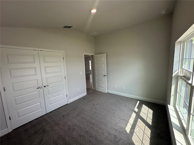 unfurnished bedroom featuring carpet, baseboards, visible vents, lofted ceiling, and a closet