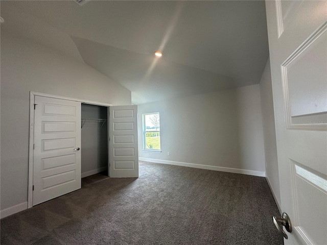 unfurnished bedroom featuring baseboards, lofted ceiling, a closet, and dark carpet