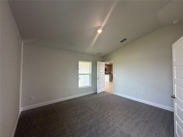 unfurnished room featuring visible vents, dark carpet, baseboards, and vaulted ceiling