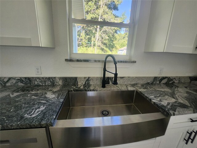 room details with dark stone countertops, white cabinetry, and sink