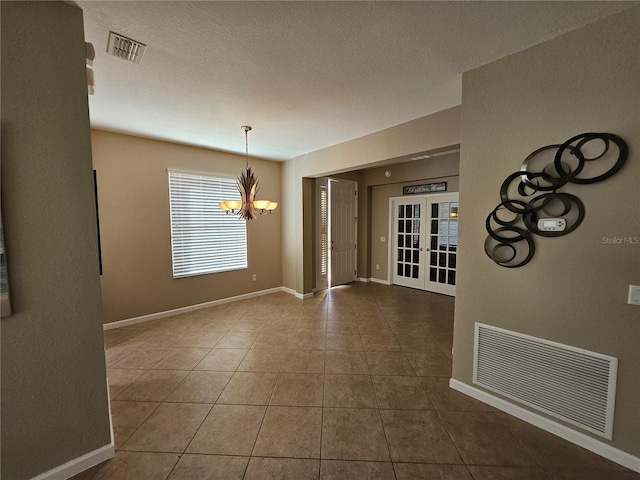 unfurnished dining area with tile patterned floors, french doors, a textured ceiling, and an inviting chandelier